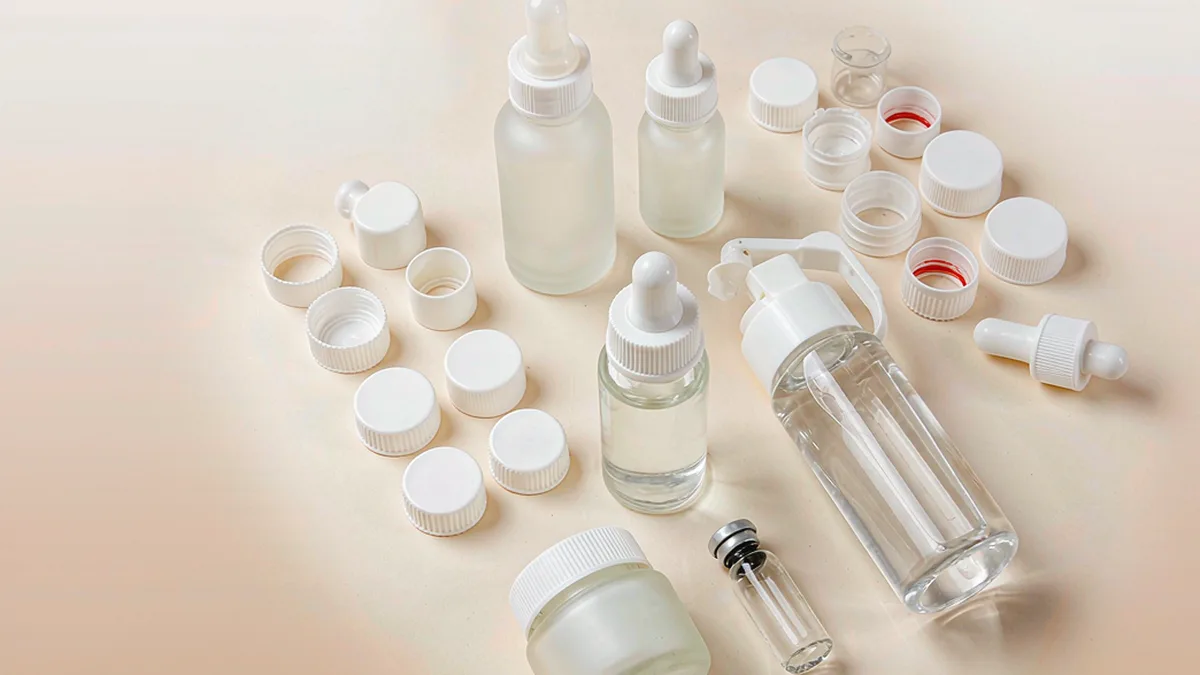 Flat-lay of child-resistant closures safe-snap squeeze-turn and CRC dropper with small cosmetic bottles