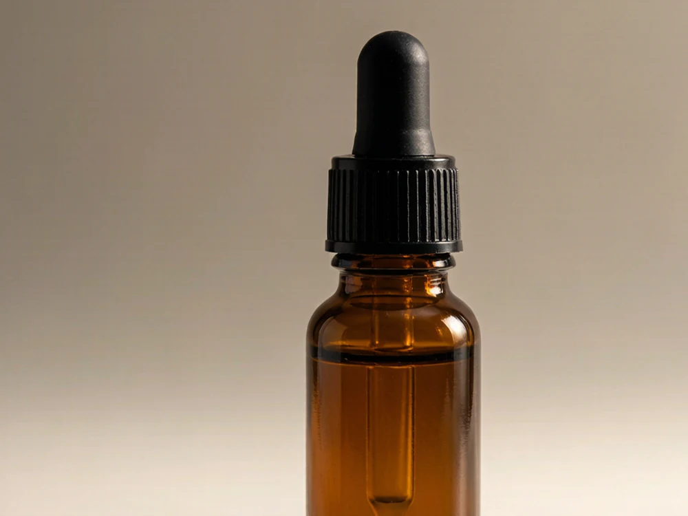 Macro of a single amber glass dropper bottle with black cap and rubber bulb on a neutral background