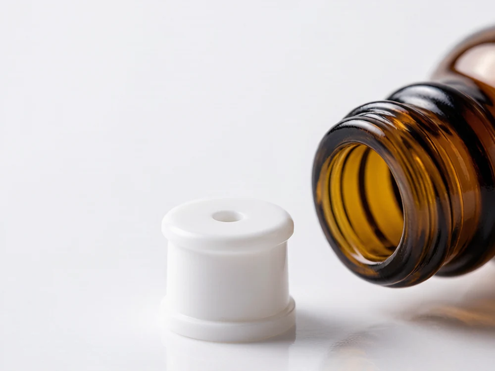 Macro of a white plastic orifice reducer insert beside an open dropper bottle neck