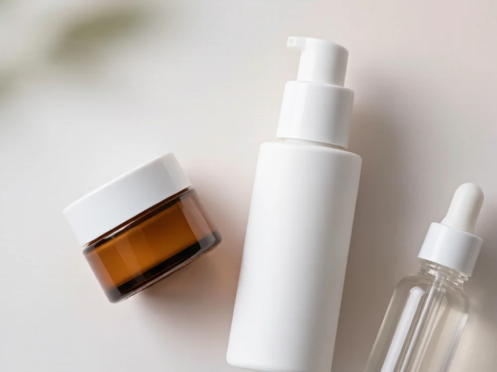 Flat lay of a white airless pump bottle, small amber jar and clear dropper bottle