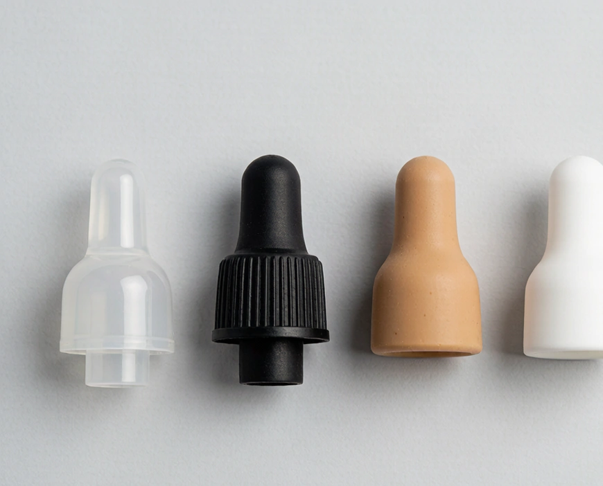 Flat-lay comparison of four dropper bulb materials on surface: silicone, nitrile, natural rubber, TPE