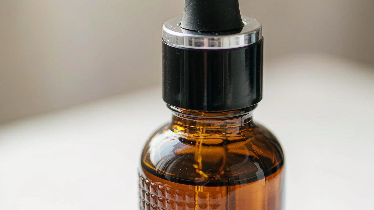 Macro close-up of an amber glass dropper serum bottle focusing on the glass cap and neck detail