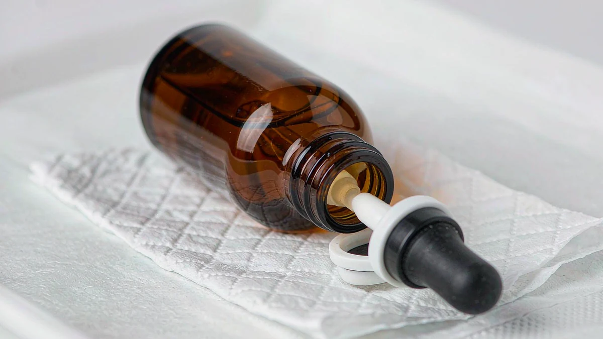 A filled amber glass dropper bottle turned upside down on white tissue paper as a leak-test setup