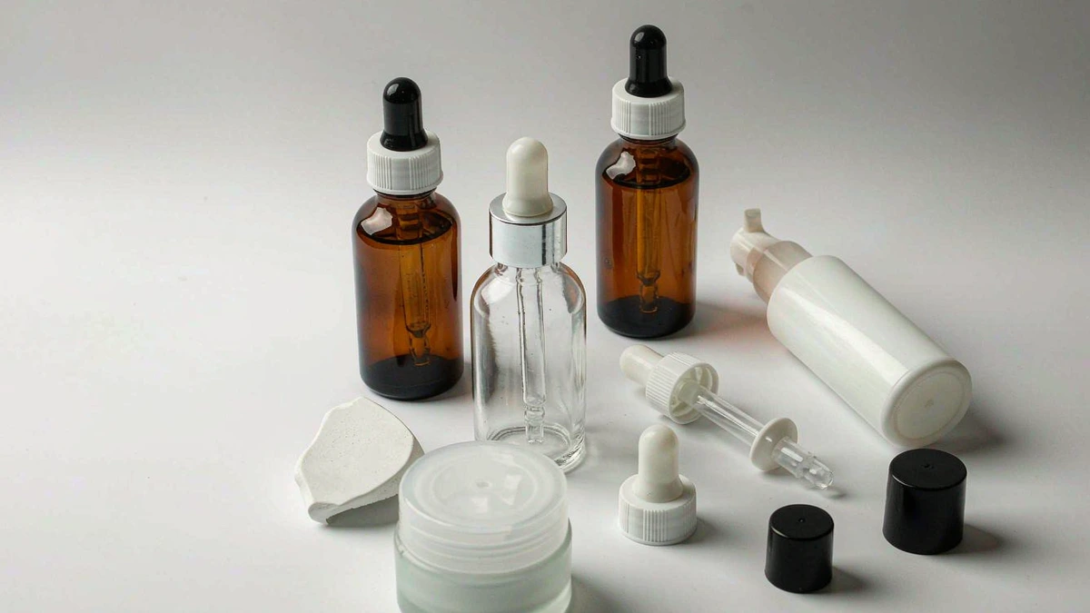 Assortment of cosmetic packaging samples - glass bottles, jars, and a pump - laid out on a clean studio table for evaluation