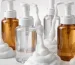 Assorted clear and amber cosmetic foam pump bottles dispensing white foam on a clean studio surface